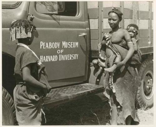 Family in Nai Nai: N!ai and a woman in front of the expedition Dodge showing "Peabody Museum of Harvard University" on the door (print is a cropped image)