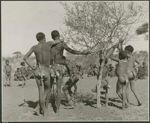 [No folder title]: People at a dance, including two men with knives in their belts, and women sitting in the background (print is a cropped image)