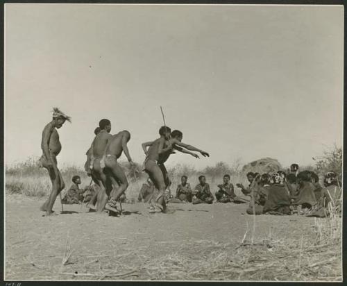 [No folder title]: Men dancing through a circle of women sitting, with one man's arms outstretched (print is a cropped image)