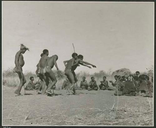 [No folder title]: Men dancing through a circle of women sitting, with one man's arms outstretched (print is a cropped image)