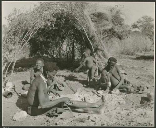 [No folder title]: Gao of Band 2 sitting by his fire with his two wives, Be (behind him) and Khuan//a (right). Khuan//a is cracking a tsi nut. (print is a cropped image)