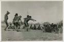 [No folder title]: Men dancing through a circle of women sitting, one stretches out his arms (print is a cropped image)