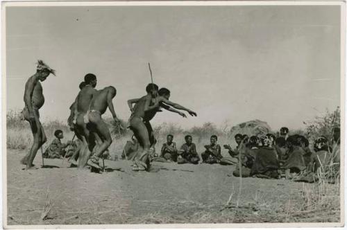 [No folder title]: Men dancing through a circle of women sitting, one stretches out his arms (print is a cropped image)