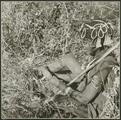 [No folder title]: Woman holding her digging stick and veldkos, and sitting next to the hole in the ground (print is a cropped image)