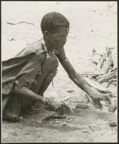 [No folder title]: "Old Xama" pounding a piece of animal skin with a fire paddle (print is a cropped image)