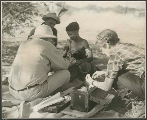 [No folder title]: Laurence Marshall putting a bandage on /Khoa's ("Qui Hunter's" daughter) burned leg, while /Naoka (her mother) gives her medicine (print is a cropped image)