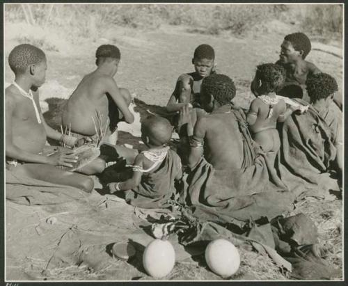 [No folder title]: Group of people sitting around a fire, including "Gao Medicine," Di!ai, "Little /Gaishay," and "≠Gao Lame" playing the //guashi (print is a cropped image)