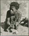 [No folder title]: ≠Toma crouching and holding a soapstone pipe (print is a cropped image)