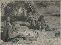 Gao of Band 2 sitting by his fire with his two wives, Be (behind him) and Khuan//a (right); Khuan//a is cracking a tsi nut (print is a cropped image)

