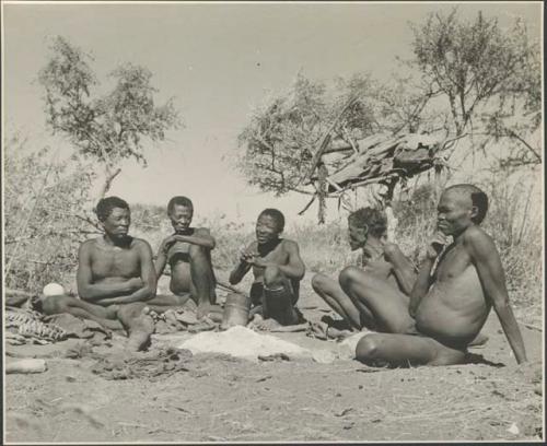 "Old ≠Toma" of Band 2, ≠Gao (husband of Khwo//o-/Gasa, brother of "Old Gau") of Band 4, "Old /Gaishay" of Band 3 and "/Qui Navel" of Band 1 sitting with "Old Gau" around the ashes of his fire
