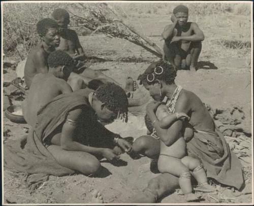 Group of people seated, with a woman holding her child on her lap in the foreground