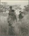 Woman with a child on her shoulders, walking with a woman carrying a load of grass and a baby on her back