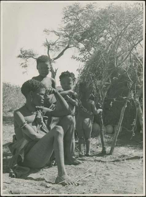 /Naoka (first wife of /Ti!kay of Band 9) sitting, with her two children, !Nani and /Khoa, and another child standing next to her
