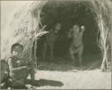 Child sitting next to a skerm, with two children standing inside it