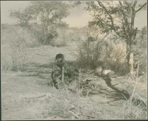 ≠Toma's sister with her child beside her, pounding something with mortar and pestle


