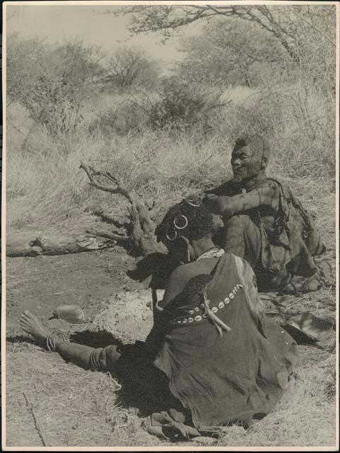 "Old Demi" and woman from /Ti!kay's group by fire; woman's kaross decorated with cowrie shells