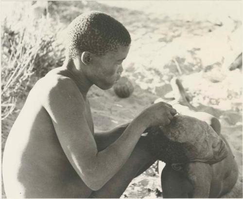 !Gai seated in profile, cutting another man's hair, close-up

