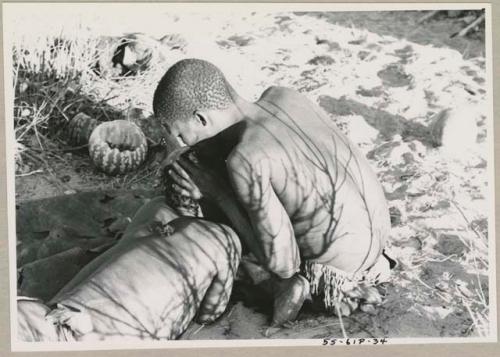 !Gai seated, cutting another man's hair, seen from the back

