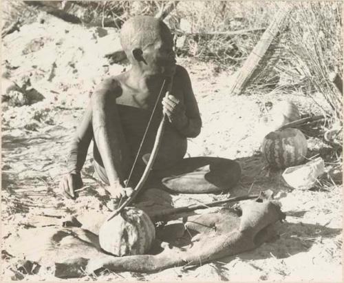 Oukwane playing a musical bow, seated
