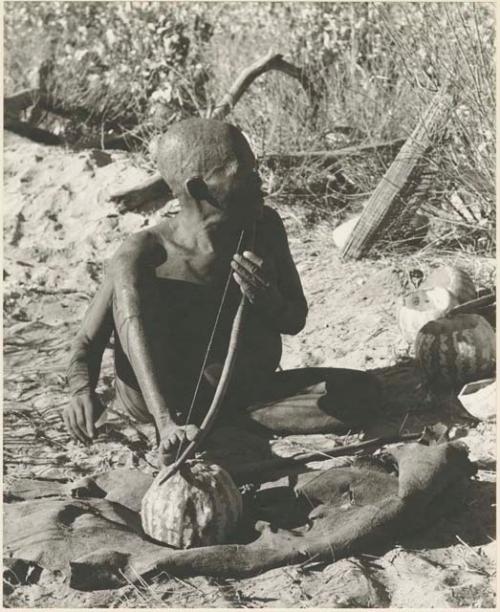 Oukwane playing a musical bow, seated
