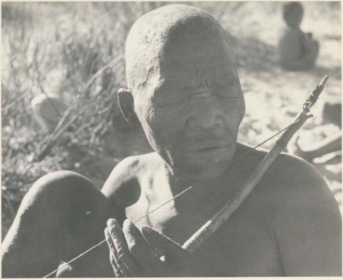 Close-up of Oukwane playing a musical bow, seated
