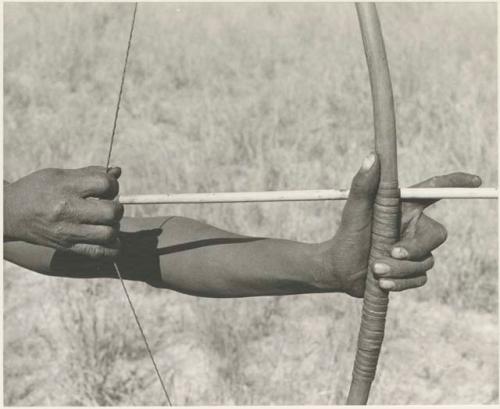 Close-up of !Gai's hands demonstrating arrow release
