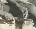 Close-up of !Gai's hands shaping an arrow point made of bone




