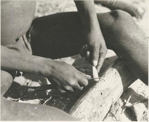 Close-up of !Gai's hands, shown sharpening a piece of bone



