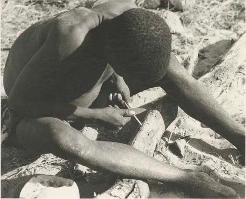 !Gai sharpening a piece of bone, full seated figure



