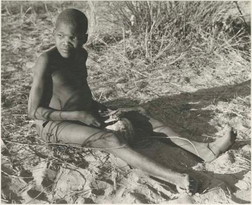 !Oukabe seated, playing a sanza placed on empty melon rind for sounding board



