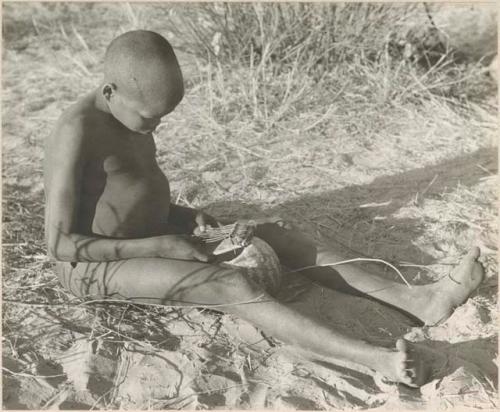 !Oukabe seated playing a sanza placed on empty melon rind used as a sounding board



