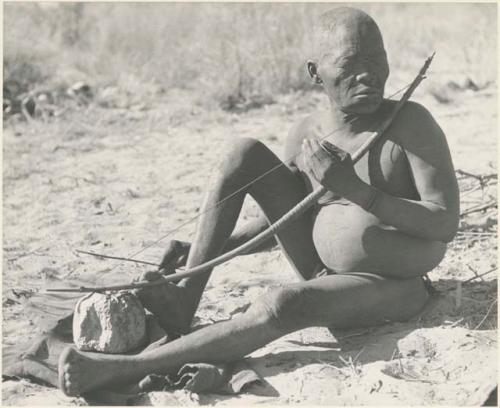 Oukwane seated, playing a bow under a tree

