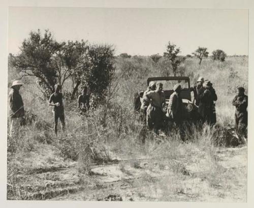 Oukwane, !Gai, and expedition members standing around expedition Jeep