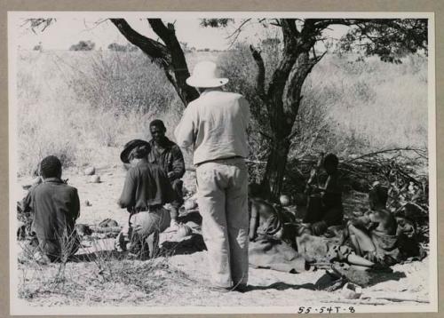 People sitting under a tree, and Laurence Marshall walking toward a group of expedition members
