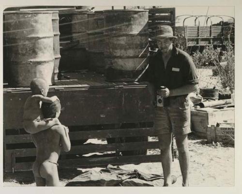 Boy carrying N!whakwe on his shoulders toward Casper Kruger standing at the back of an expedition truck (GMC)
