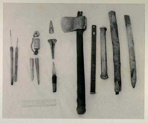 Metal objects among /Twikwe's possessions, including a nail-like piece of metal thrust into a stick used to sharpen knives, an awl for sewing, 2 pipes from cartridge shells, a fire-striker, a knife belonging to //Kwai≠kabe (her son), a piece of bone or duiker horn, an axe belonging to her husband, a metal piece he found which he will hammer into an implement, a metal pounding rod, and two scrapers made from an old knife blade, with a ruler for measurement