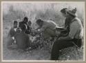 Oukwane and other people sitting and talking to William Donnellan and Elizabeth Marshall Thomas, with Wilhelm Camm interpreting. Oukwane is naming the internal parts of an animal