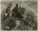 Oukwane and other people sitting and talking to William Donnellan and Elizabeth Marshall Thomas, with Wilhelm Camm interpreting. Oukwane is naming the internal parts of an animal