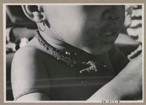 N!whakwe wearing a necklace and earring, close-up