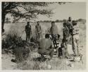 Members of a visiting band from Okwa sitting and standing under a tree, with Kernel Ledimo and Lorna Marshall
