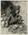 Tsekue taking tsama melons out of her kaross, with /Twikwe and Oukwane behind her