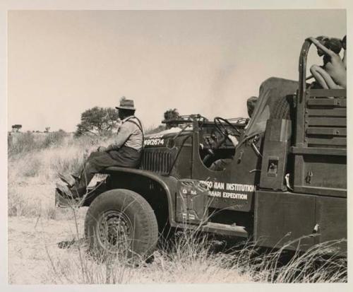 Children riding on the top of an expedition truck (GMC), and Wilhelm Camm riding on the fender, with a group of people standing under a tree in the distance