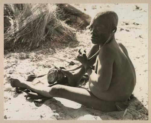 Oukwane seated, playing a bow, seen from behind

