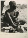 Oukwane seated, playing a bow
