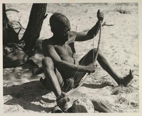 Oukwane seated, playing a musical bow
