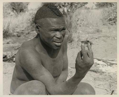 Visiting man demonstrating hunting hand signals, half figure seated
