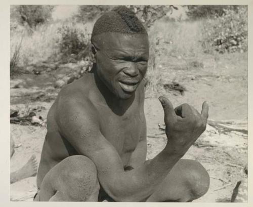 Visiting man demonstrating hunting hand signals, half figure seated