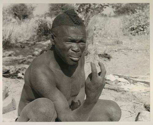 Visiting man demonstrating hunting hand signals, half figure seated
