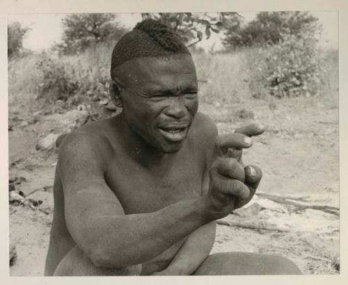 Visiting man demonstrating hunting hand signals, half figure seated

