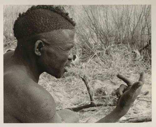 Visiting man demonstrating hunting hand signals, half figure seated
